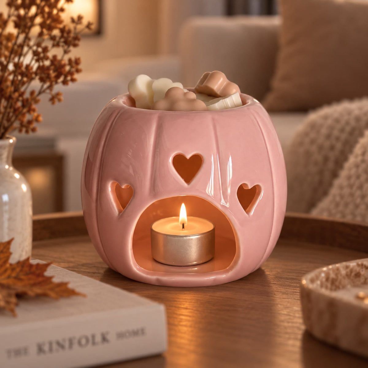 Quemador de wax melts de cerámica rosa encendido con vela de té en ambiente otoñal